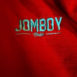 Burgundy pullover hoodie sweatshirt with "Jomboy Media" embroidered in blue